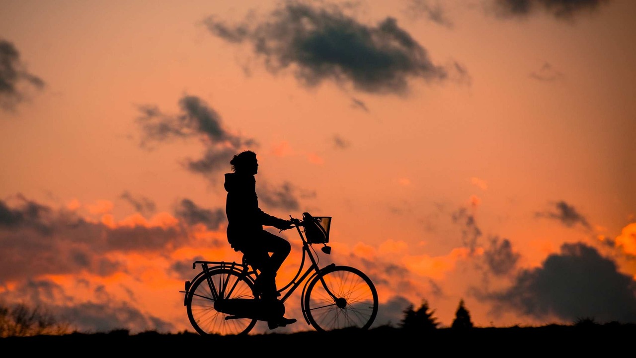 Cyclist silhouetted against an orange sunset sky