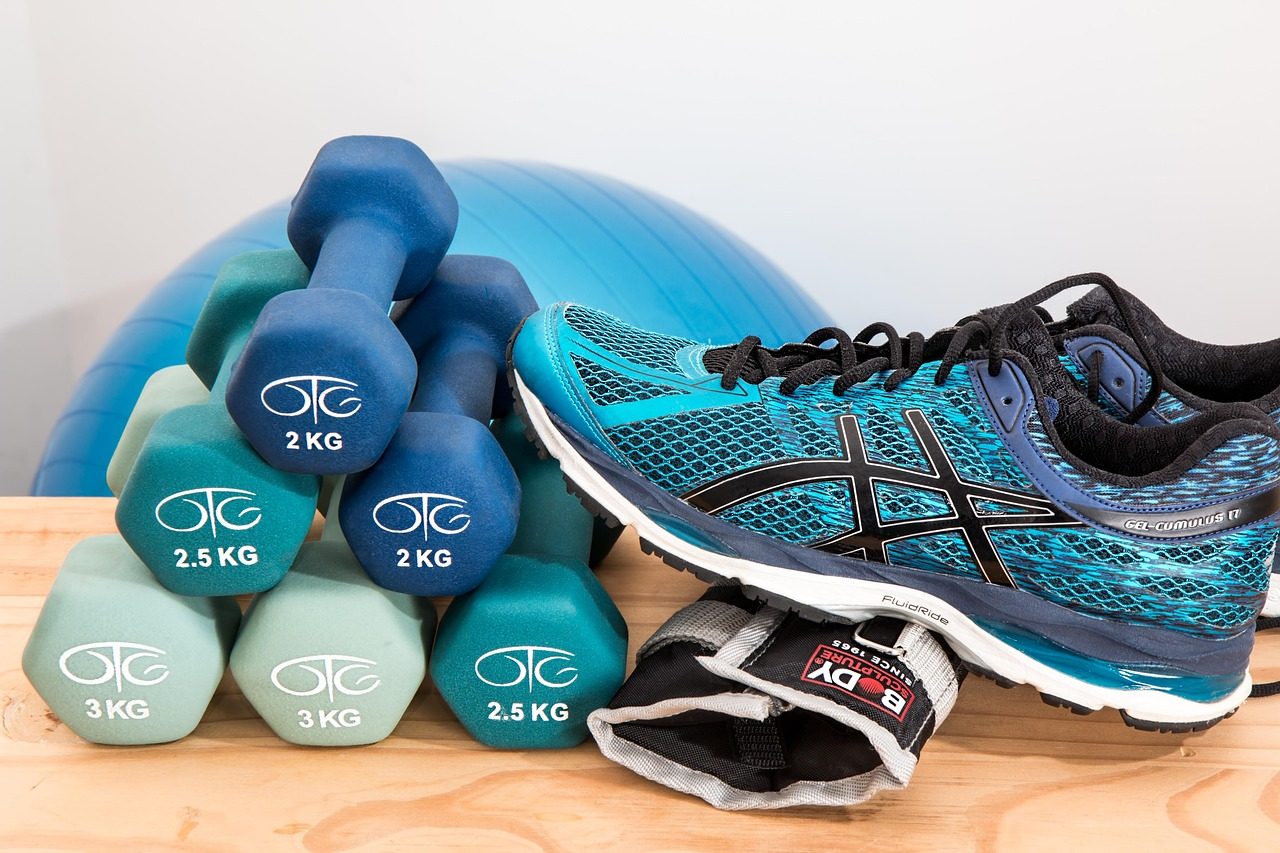 Light dumbbells, an exercise ball and running shoes on a wooden floor