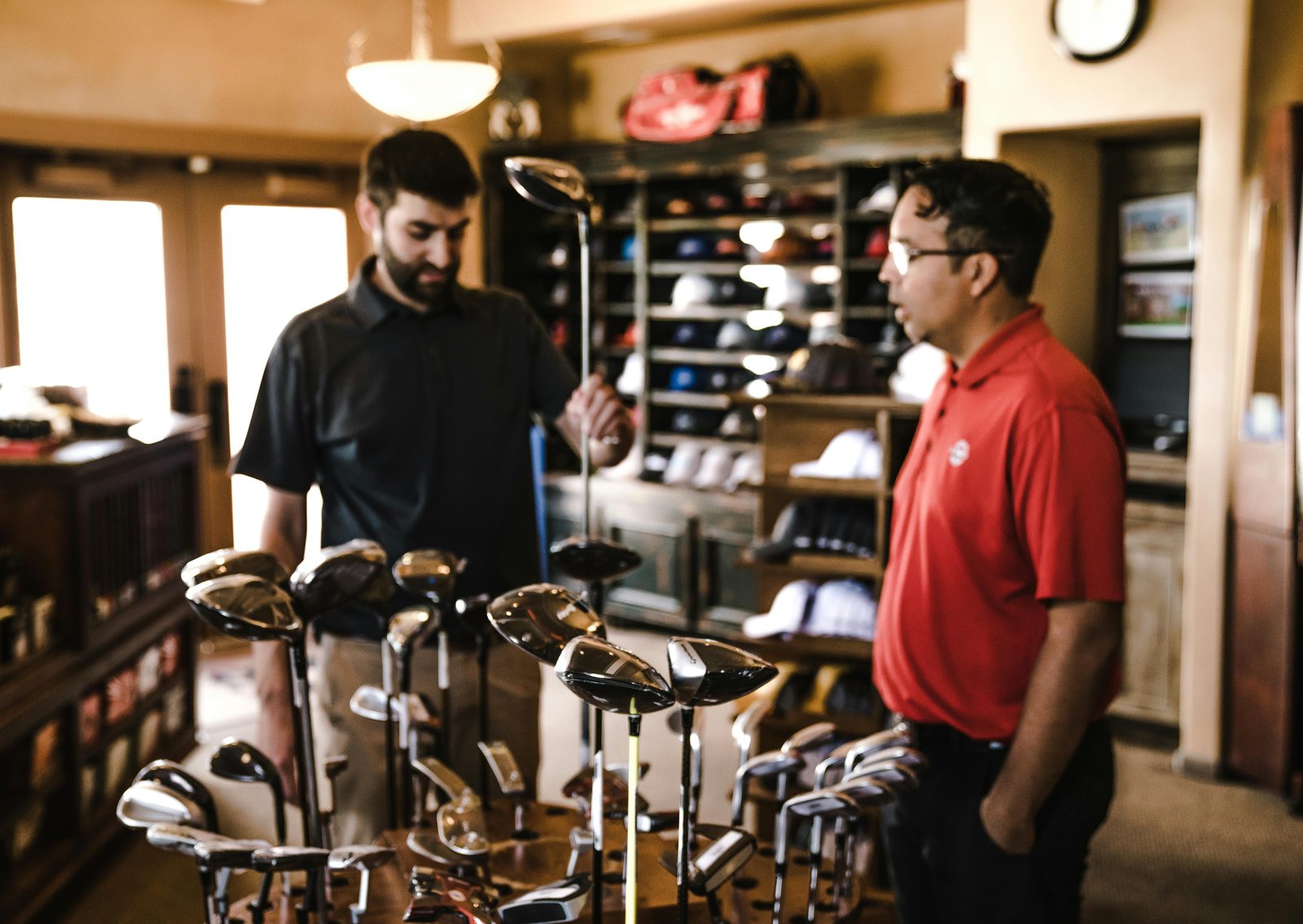 Two men talking over a display of golf clubs in a sports shop
